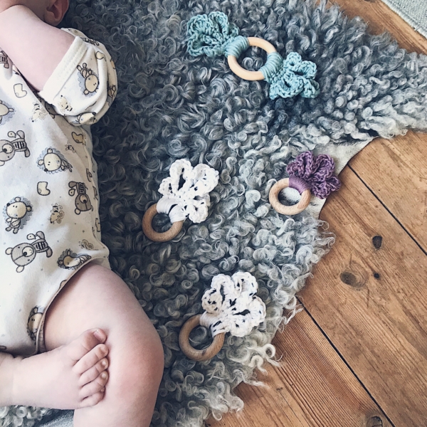 A baby is laying on a short haired sheepskin with four of the LoLo Loop Baby teether