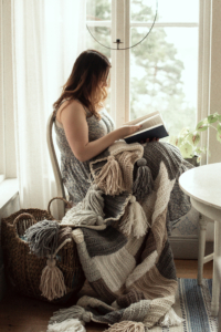 Tess sitting and reading infront of a window with the Stay Awhile Boho Blanket