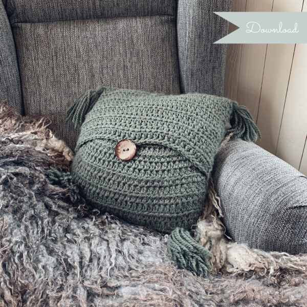 A moss green Stay Awhile Boho Pillow placed in an armchair