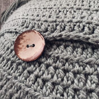A closeup picture of a large wooden button on the Stay Awhile Boho Pillow